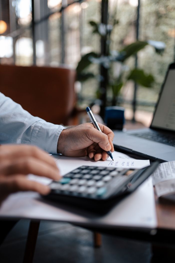 why-choose-us A person calculating finances with a calculator and pen on a desk indoors.