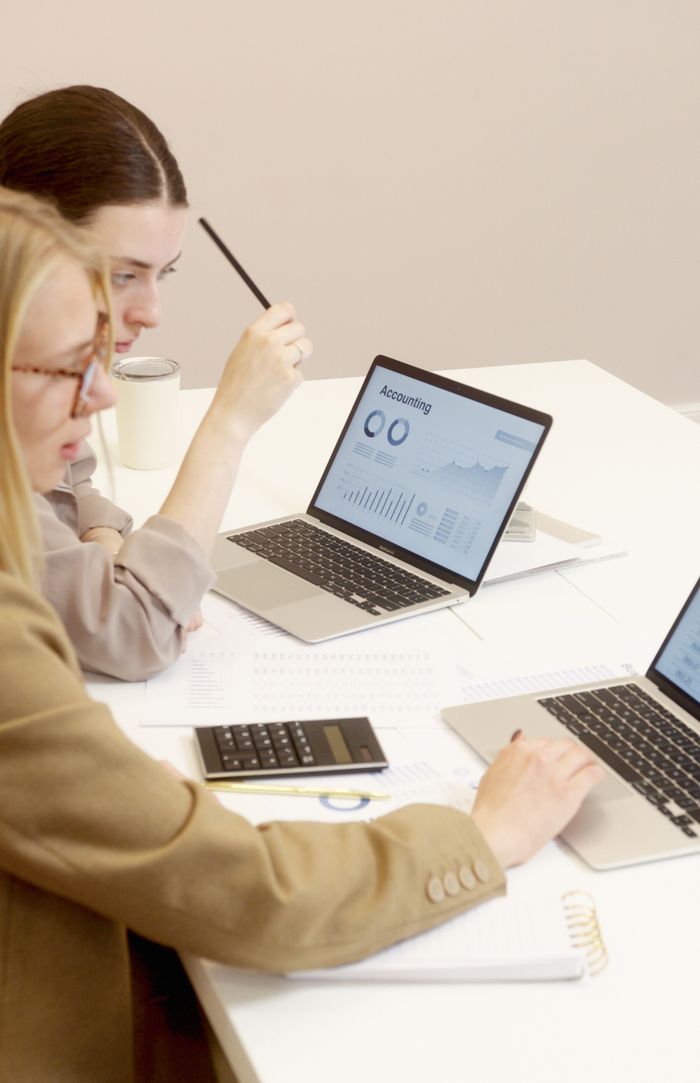 creative-03 Two women collaborate on financial data analysis with laptops in an office setting.