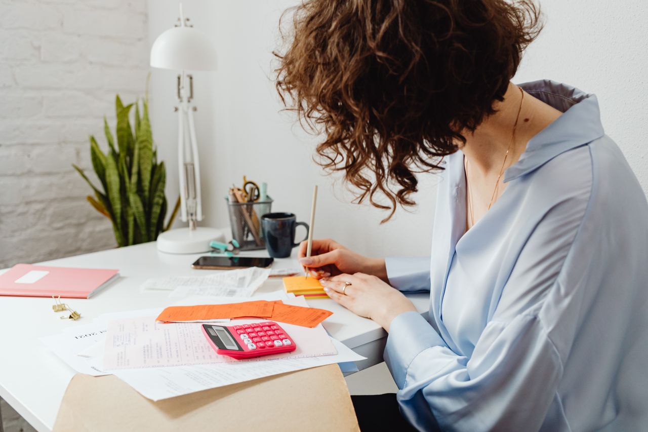 creative-02 Woman writing with calculator on desk, managing finances indoors.